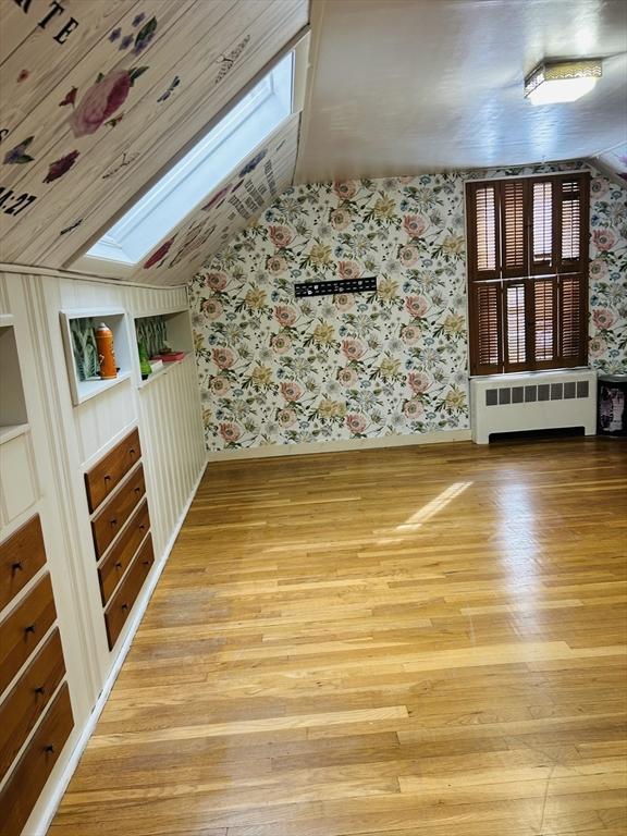 bonus room featuring built in features, radiator heating unit, a skylight, and light wood-type flooring