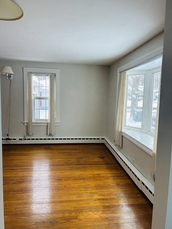 empty room with hardwood / wood-style flooring and a baseboard radiator