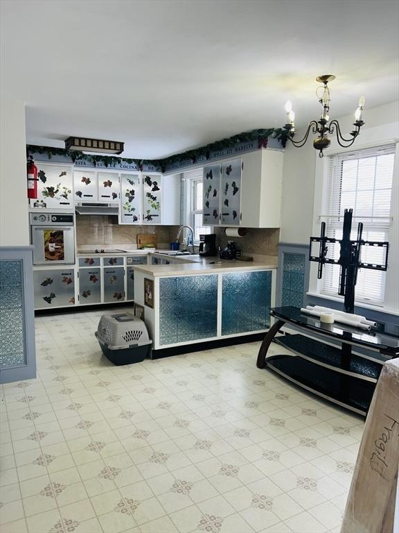 kitchen featuring white cabinets, decorative backsplash, hanging light fixtures, a chandelier, and oven