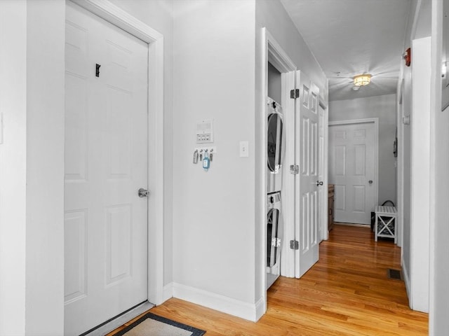 hallway featuring visible vents, light wood-style flooring, baseboards, and stacked washing maching and dryer