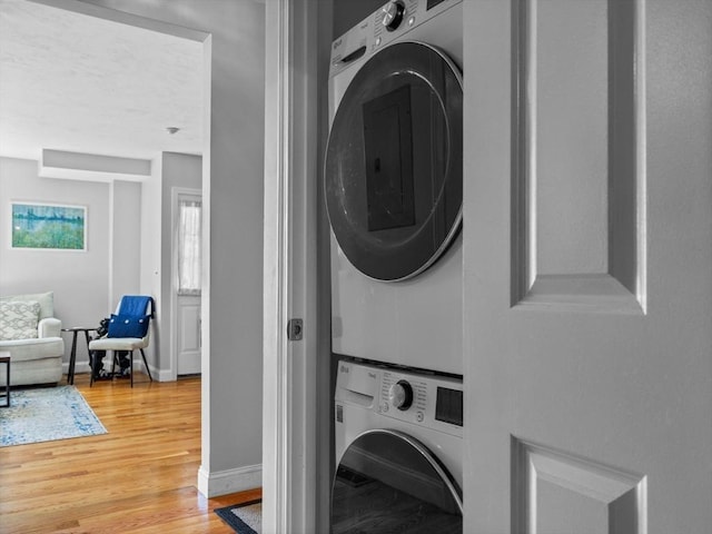 washroom featuring baseboards, wood finished floors, stacked washer and clothes dryer, and laundry area