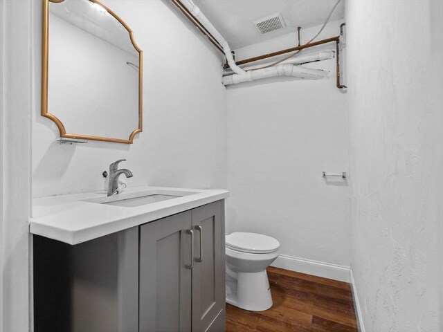 bathroom featuring wood finished floors, visible vents, toilet, vanity, and baseboards