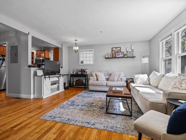 living room with wood finished floors, electric panel, baseboards, and a notable chandelier