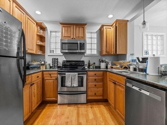 kitchen featuring brown cabinets, stainless steel appliances, dark countertops, a sink, and light wood-style flooring