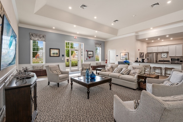 carpeted living room featuring a raised ceiling and ornamental molding