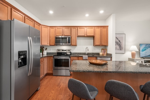 kitchen with appliances with stainless steel finishes, a breakfast bar area, light wood-type flooring, a center island, and sink