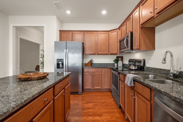 kitchen featuring wood-type flooring, dark stone countertops, appliances with stainless steel finishes, and sink