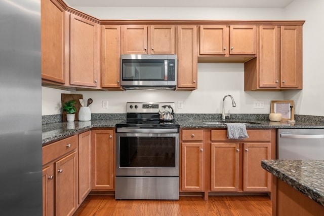 kitchen featuring appliances with stainless steel finishes, light hardwood / wood-style floors, dark stone countertops, and sink