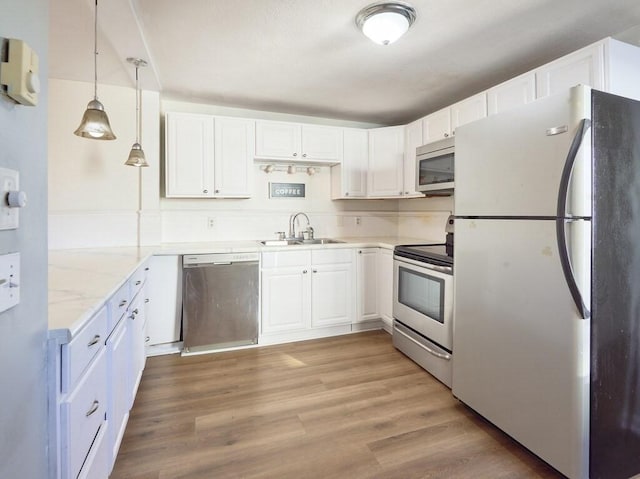 kitchen with appliances with stainless steel finishes, decorative light fixtures, white cabinets, light stone counters, and sink