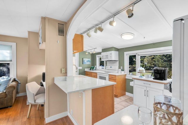 kitchen with white appliances, light hardwood / wood-style flooring, kitchen peninsula, and white cabinets