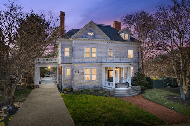 view of front of property with covered porch, a lawn, a balcony, a chimney, and concrete driveway