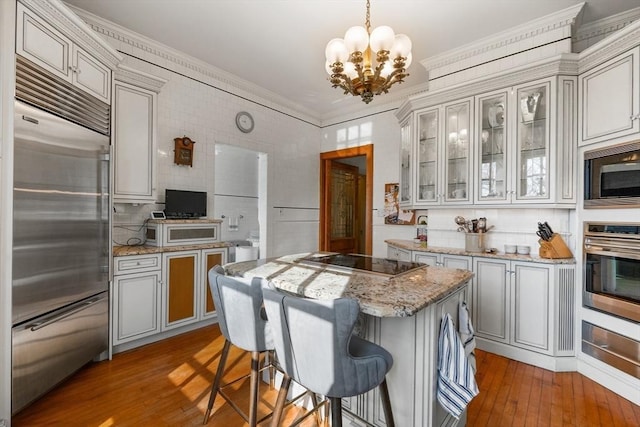 kitchen featuring glass insert cabinets, built in appliances, a chandelier, a warming drawer, and light wood-style flooring