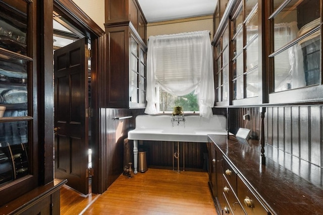 kitchen featuring light wood-type flooring, built in study area, glass insert cabinets, and dark countertops
