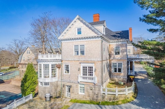 rear view of house featuring a chimney, fence, and a balcony