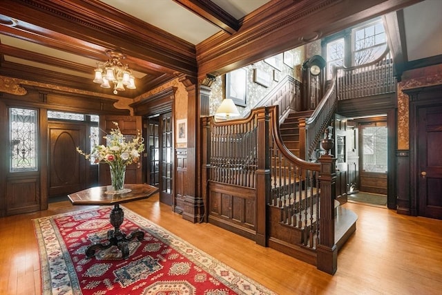 entrance foyer featuring an inviting chandelier, beamed ceiling, ornamental molding, stairway, and wood finished floors
