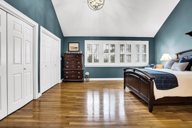 bedroom featuring multiple closets, lofted ceiling, a notable chandelier, and hardwood / wood-style flooring