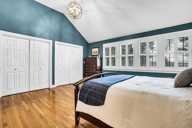 bedroom with lofted ceiling, hardwood / wood-style flooring, two closets, and an inviting chandelier