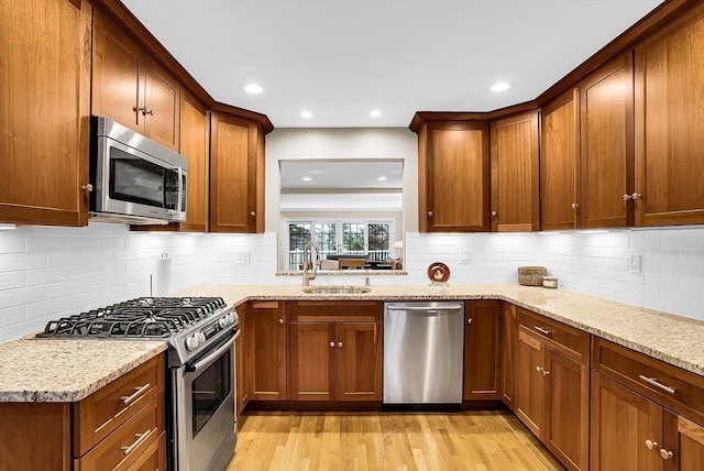 kitchen with sink, light stone countertops, stainless steel appliances, and light wood-type flooring