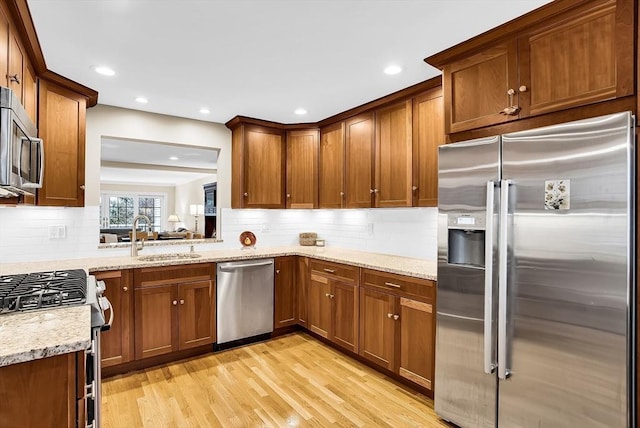 kitchen with sink, stainless steel appliances, tasteful backsplash, light stone counters, and light wood-type flooring