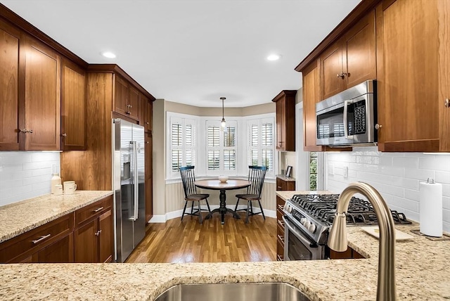 kitchen with light wood-type flooring, appliances with stainless steel finishes, tasteful backsplash, decorative light fixtures, and light stone counters