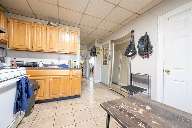 kitchen featuring gas range gas stove, a drop ceiling, light tile patterned floors, and sink