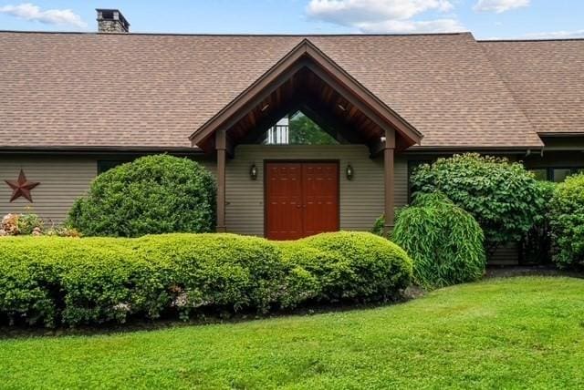 property entrance with a yard, roof with shingles, and a chimney