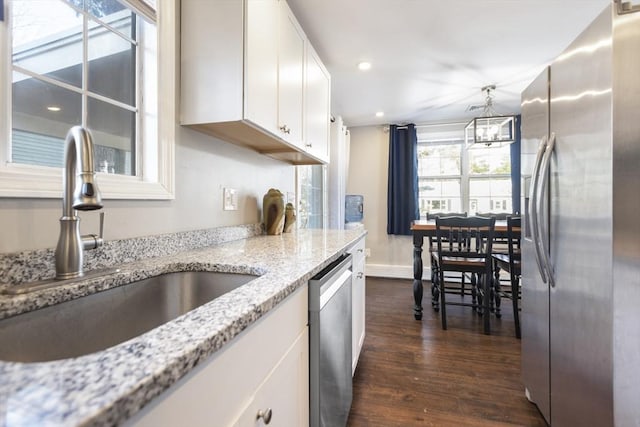 kitchen with dark wood finished floors, stainless steel appliances, a notable chandelier, white cabinetry, and a sink