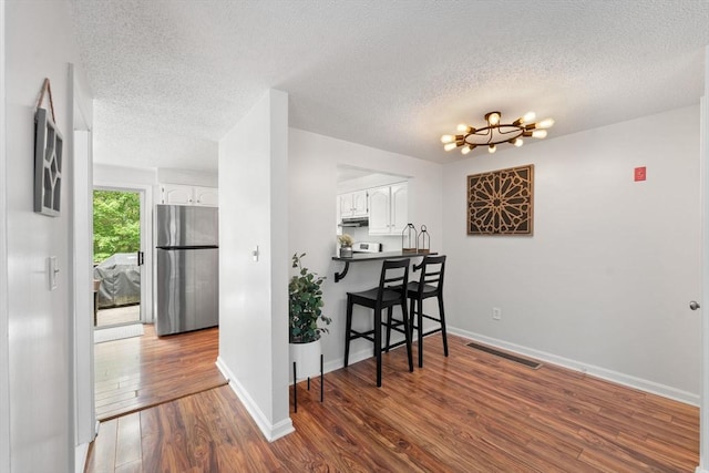 2 Colonial Dr Unit 2, Norton, MA 02766 - kitchen with freestanding refrigerator, a textured ceiling, white cabinetry, wood finished floors, and a kitchen bar