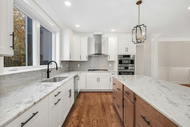 kitchen featuring sink, wall chimney exhaust hood, light stone counters, white cabinetry, and stainless steel appliances