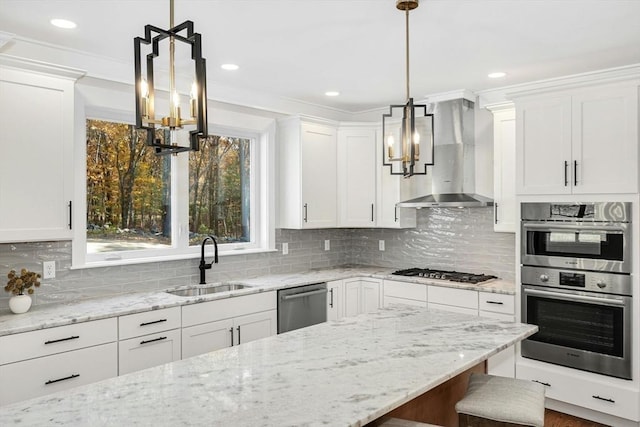 kitchen with white cabinets, sink, decorative light fixtures, and wall chimney range hood