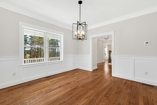 unfurnished dining area featuring hardwood / wood-style flooring, crown molding, and an inviting chandelier