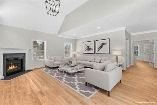 living room with a notable chandelier, light hardwood / wood-style floors, ornamental molding, and vaulted ceiling