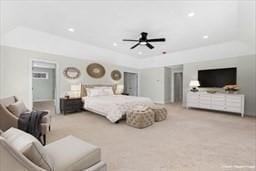 bedroom with light colored carpet, a raised ceiling, and ceiling fan