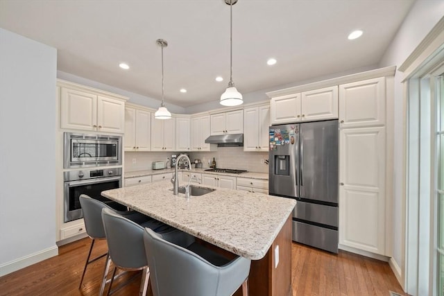 kitchen featuring decorative backsplash, dark wood-style floors, under cabinet range hood, a sink, and stainless steel appliances
