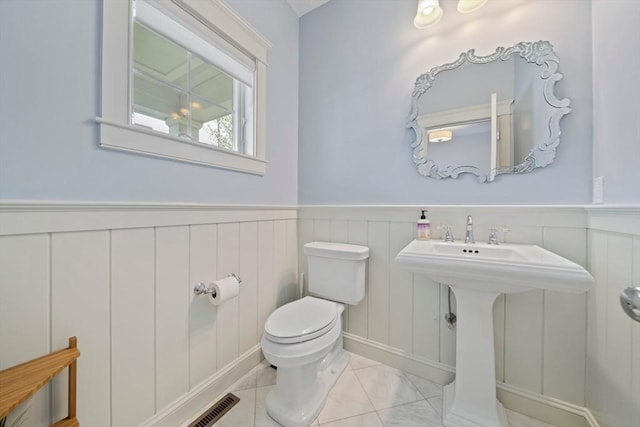 half bath with visible vents, a decorative wall, a wainscoted wall, and toilet