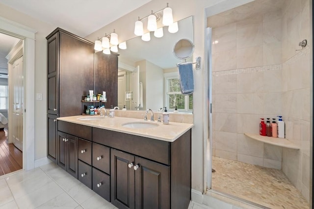 bathroom with double vanity, baseboards, tiled shower, and a sink