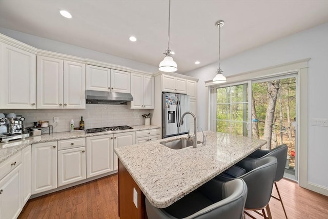 kitchen featuring backsplash, a center island with sink, a sink, under cabinet range hood, and stainless steel appliances