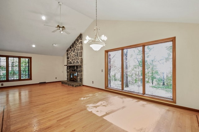 unfurnished living room featuring a stone fireplace, ceiling fan with notable chandelier, hardwood / wood-style floors, and high vaulted ceiling