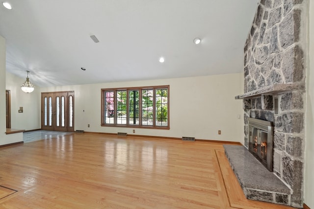 unfurnished living room featuring a stone fireplace, lofted ceiling, and hardwood / wood-style floors