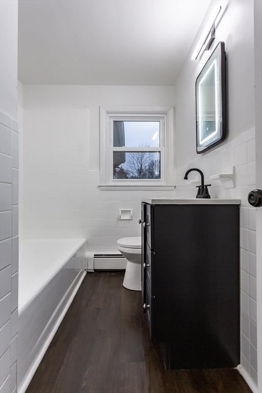 bathroom with a baseboard heating unit, wood-type flooring, toilet, vanity, and tile walls