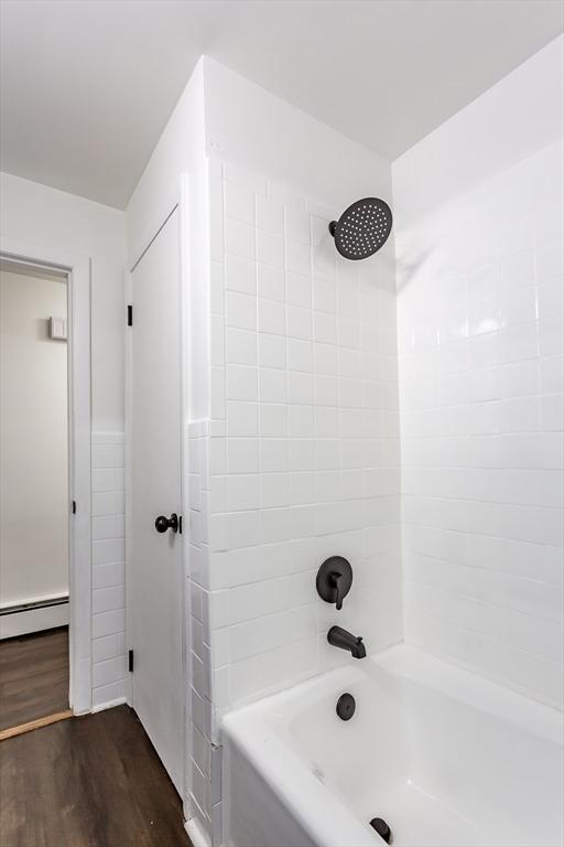 bathroom with hardwood / wood-style floors, a baseboard radiator, and tiled shower / bath