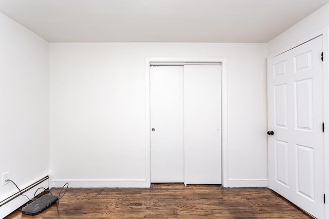 unfurnished bedroom with dark hardwood / wood-style flooring, a closet, and baseboard heating