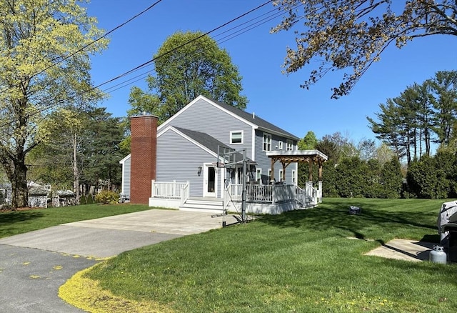 view of front of house with concrete driveway, a deck, a chimney, and a front lawn