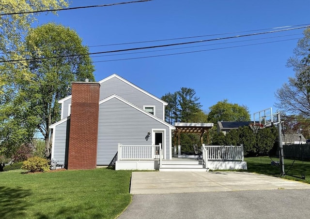 view of side of property featuring a lawn, a wooden deck, a chimney, and a pergola