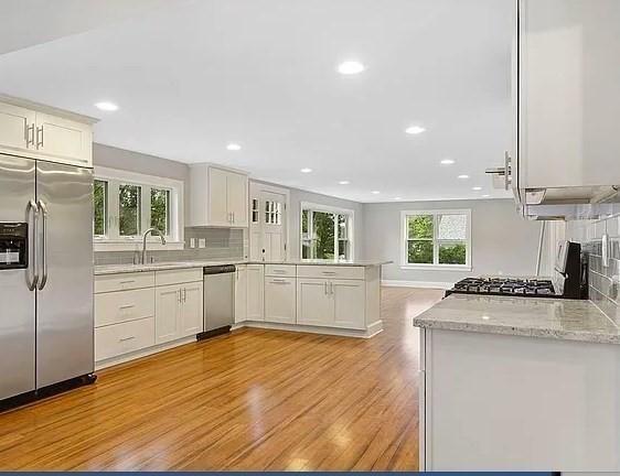 kitchen featuring light wood-style floors, stainless steel appliances, white cabinetry, a peninsula, and tasteful backsplash