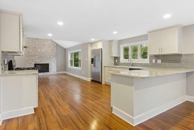 kitchen with backsplash, appliances with stainless steel finishes, light stone countertops, a peninsula, and dark wood-type flooring