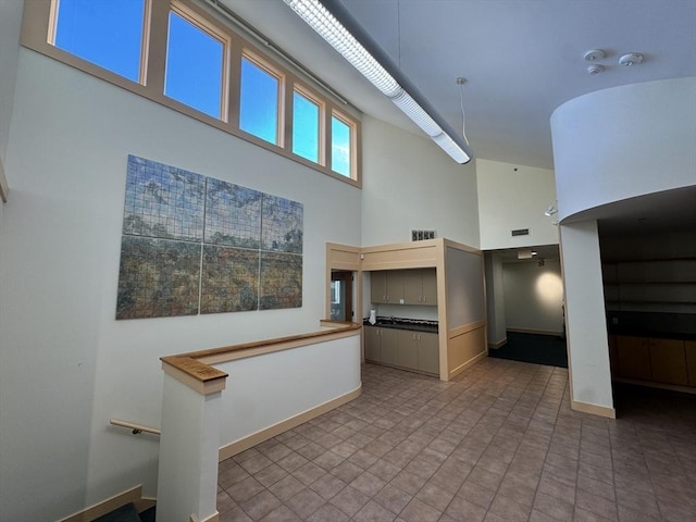 hallway with visible vents, a towering ceiling, and baseboards