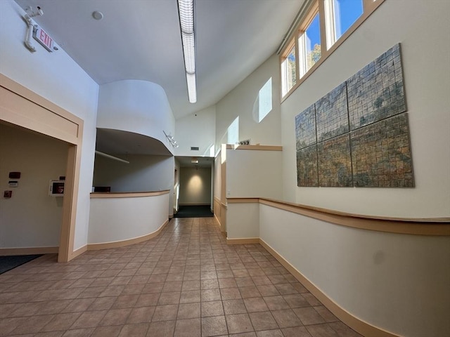 hall featuring a high ceiling, baseboards, and tile patterned floors