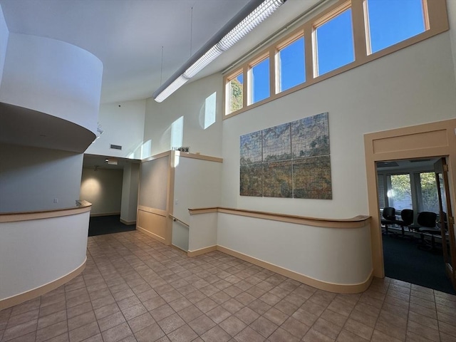 interior space with visible vents, a high ceiling, baseboards, and a wealth of natural light