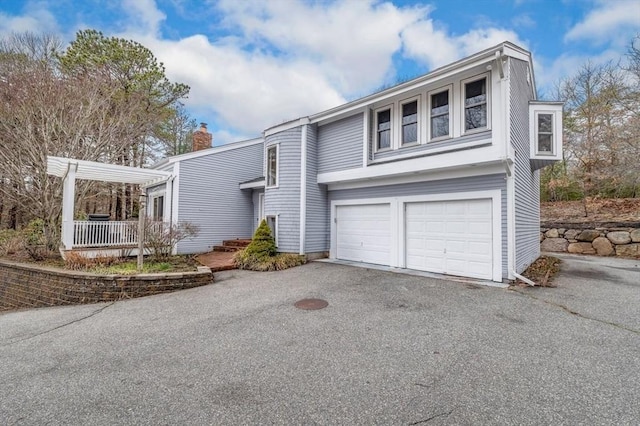 view of front facade with an attached garage, a chimney, and aphalt driveway